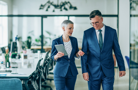 A picture of a man and woman in business attire walking in an office setting