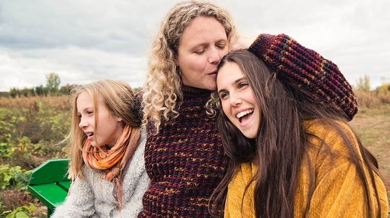 Mom with two daughters hugging within an open field photo