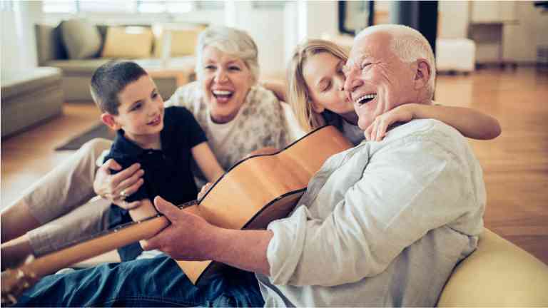 A picture of a grandpa playing a guitar while grandma and grandkids
