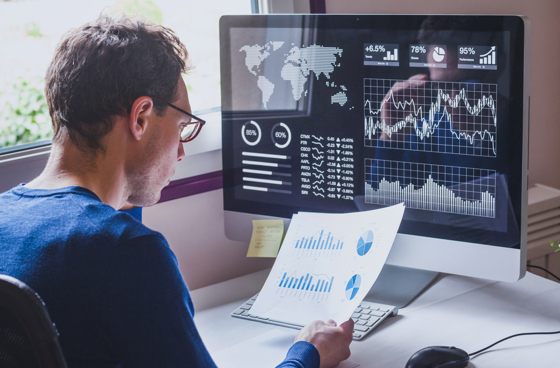 A picture of a man looking at stock reports in front of a desktop