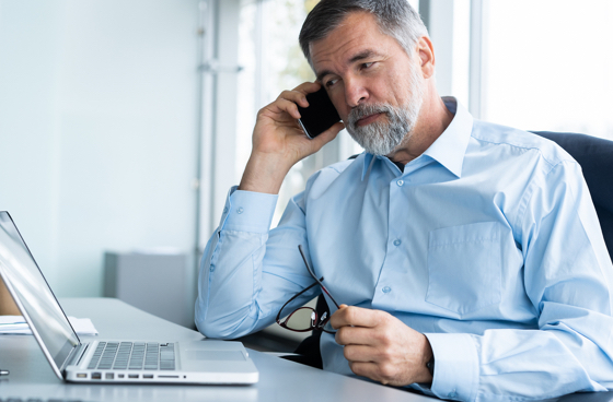 A picture of a man talking on the phone while looking at his laptop