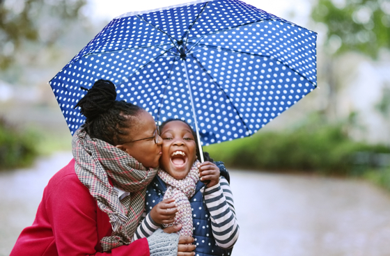 A picture of a mother and daughter holding a blue umbrella enjoying the rain