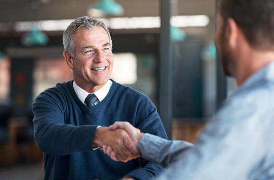 A picture showing an older man shaking hands with a younger man in office setting