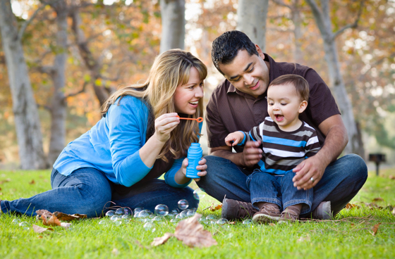 A picture of a man and woman blowing bubbles with their baby in a park