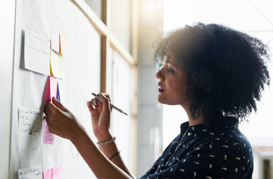 A picture of a woman writing something on a post it on a bulletin board