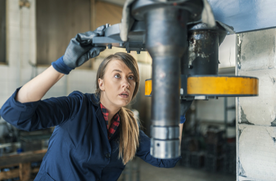 A picture of a woman looking at a machine part in a workshop